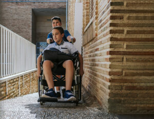 A boy pushing his friend's wheelchair up a ramp to enter school. Back to school and integration concept.