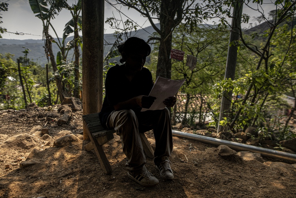 Una joven lee sentada en una silla. Se encuentra en casa, en el exterior, en algún país centroamericano. 