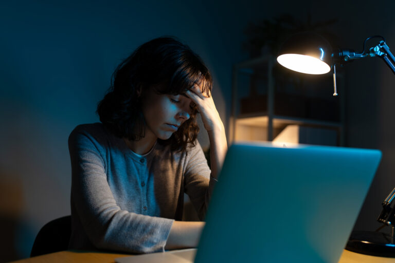 Reportaje“He visto explotación”: cuatro exmiembros de CREA hablan de su experiencia Tired woman working late at night using laptop at home office having headache. Headache and burnout concept.