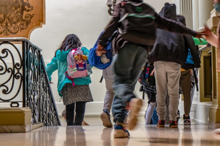 niñas y niños bajan las escaleras de su centro educativo con las mochilas a la espalda. Unos corren, otros caminan