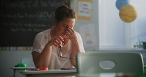 Tired Female Teacher Sitting Alone at the Desk in Empty Classroom, Relaxing After Class. Woman Feeling Stress, Burnout and Mental Exhaustion in Educational Environment, Working in Elementary School.