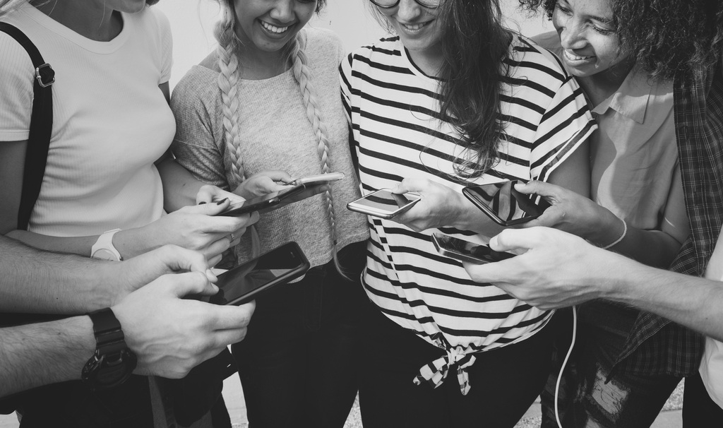 Grupo de jóvenes adultos sentados al aire libre, usando teléfonos móviles juntos en un entorno urbano.