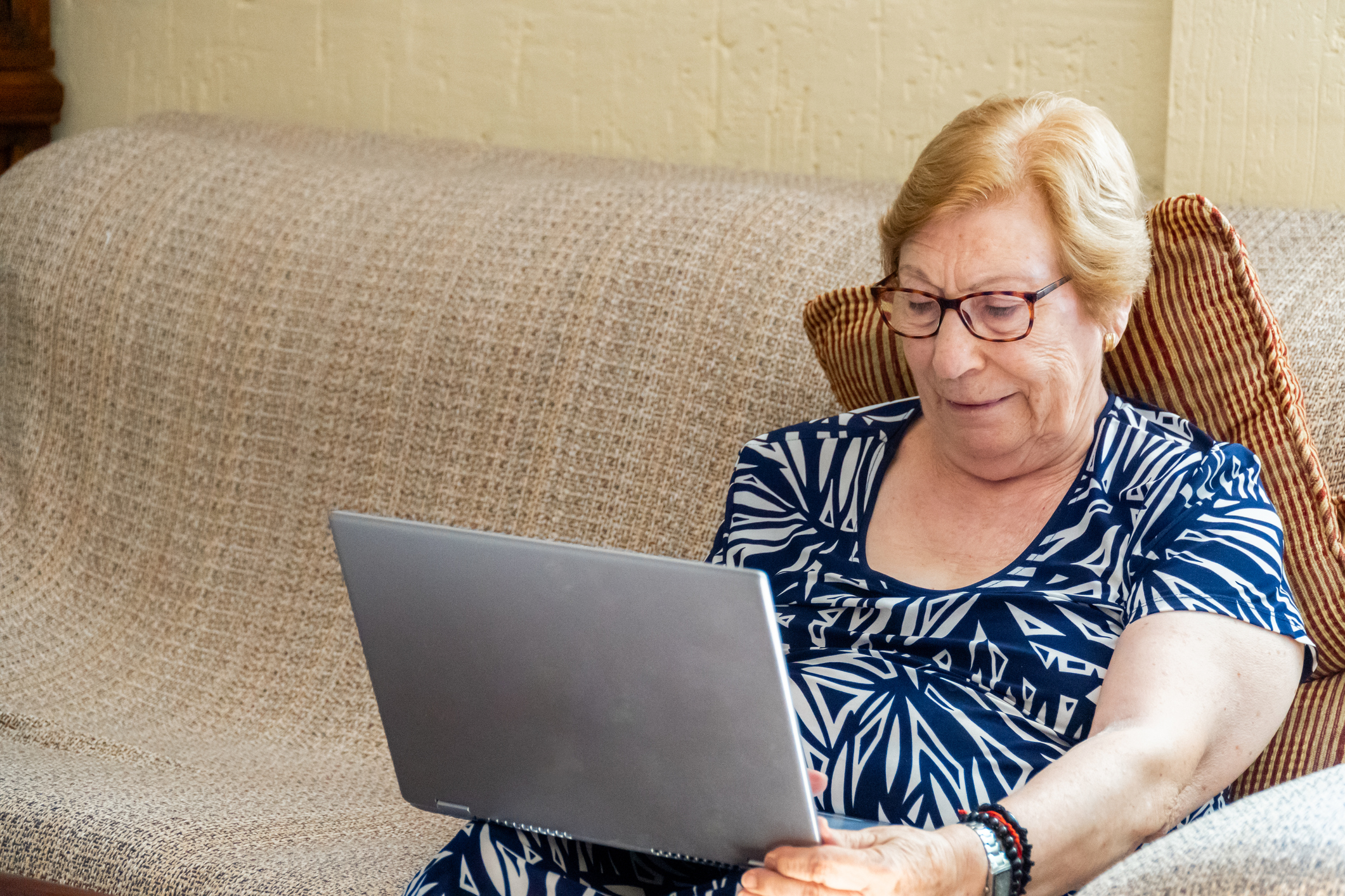 Señora mayor consulta su ordenador portátil desde el sofá